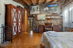 A rustic room with a wooden bed, a desk, and a chair. There is a painting on the wall and a map on the desk.
