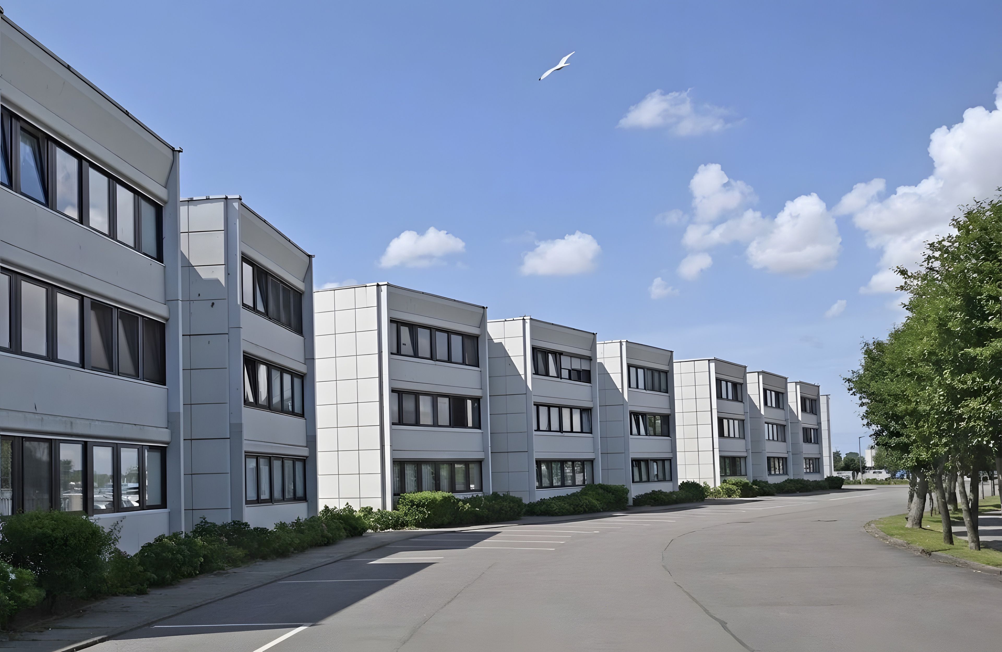 Ein modernes Gebäude mit mehreren Stockwerken, großen Fenstern und einem Parkplatz.