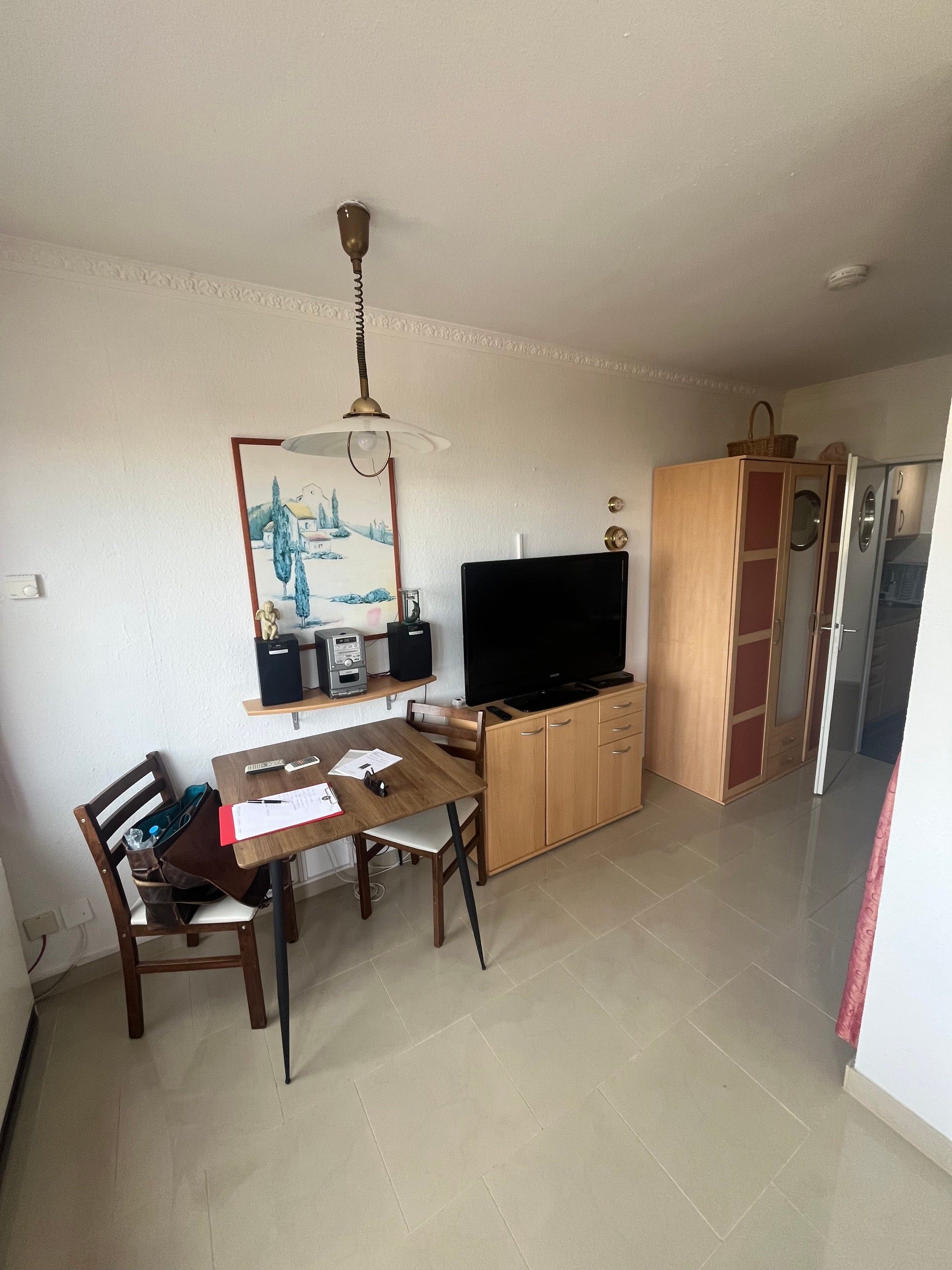 Ein kompakter Wohnraum mit Esstisch, Stühlen, Fernseher und Kleiderschrank.