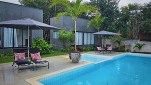 A swimming pool with lounge chairs and umbrellas, surrounded by a modern building and greenery. - Celias Beautiful House (Tibau do Sul)