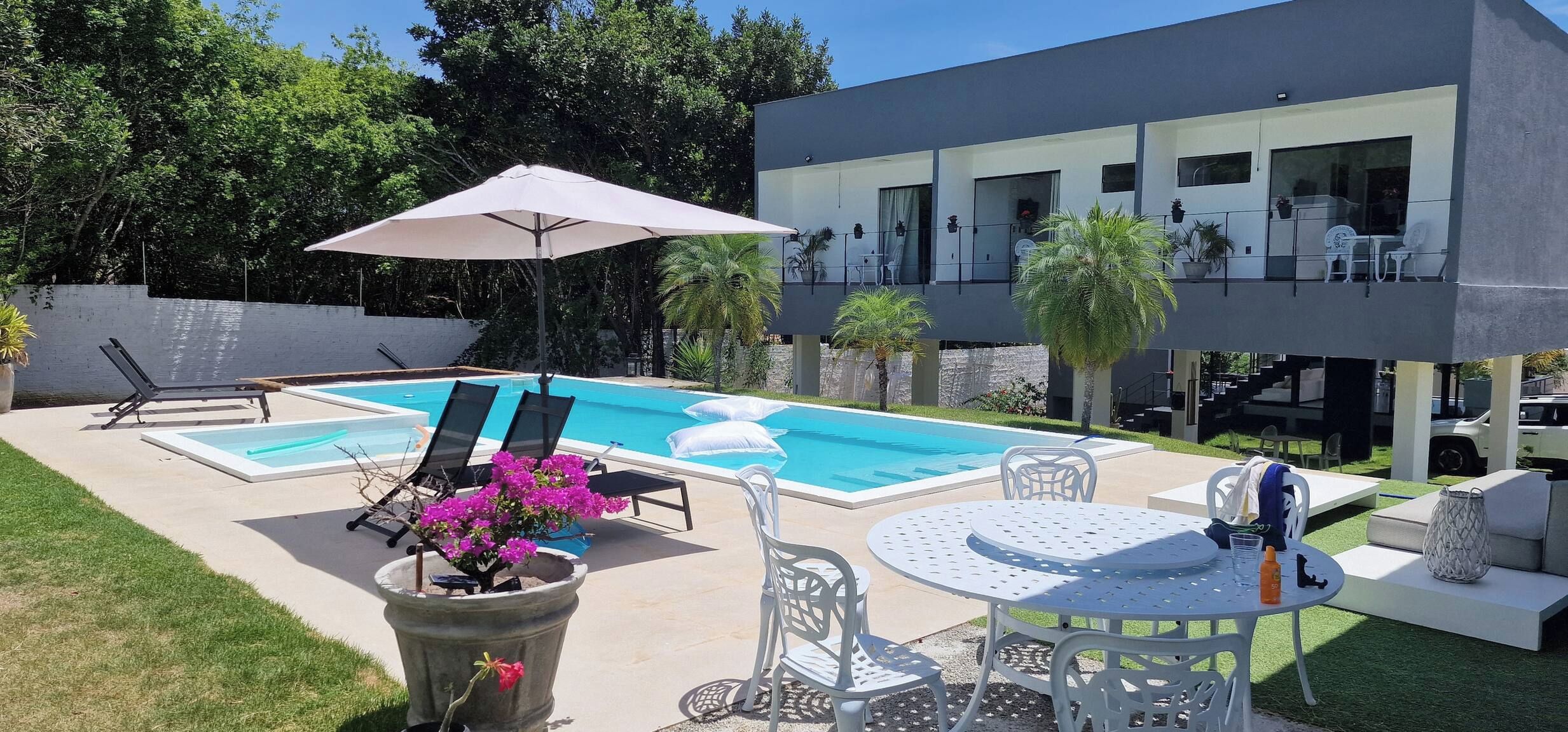 A modern outdoor pool area with lounge chairs, a table, and a large umbrella.