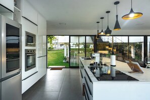 A modern kitchen with built-in appliances, large windows, and a view of the outdoors. - Celias Beautiful House (Tibau do Sul)