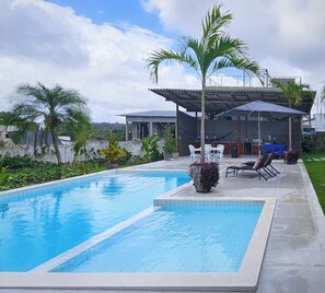 A swimming pool with a tiled deck, lounge chairs, and a covered outdoor seating area. - Celias Beautiful House (Tibau do Sul)