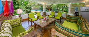 A cozy outdoor seating area with a pool view, green chairs, a wooden table, and a striped cushion.