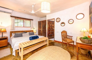 A bedroom with a bed, bedside tables, a wooden bench, a chair, a lamp, a ceiling fan, and a window with curtains.