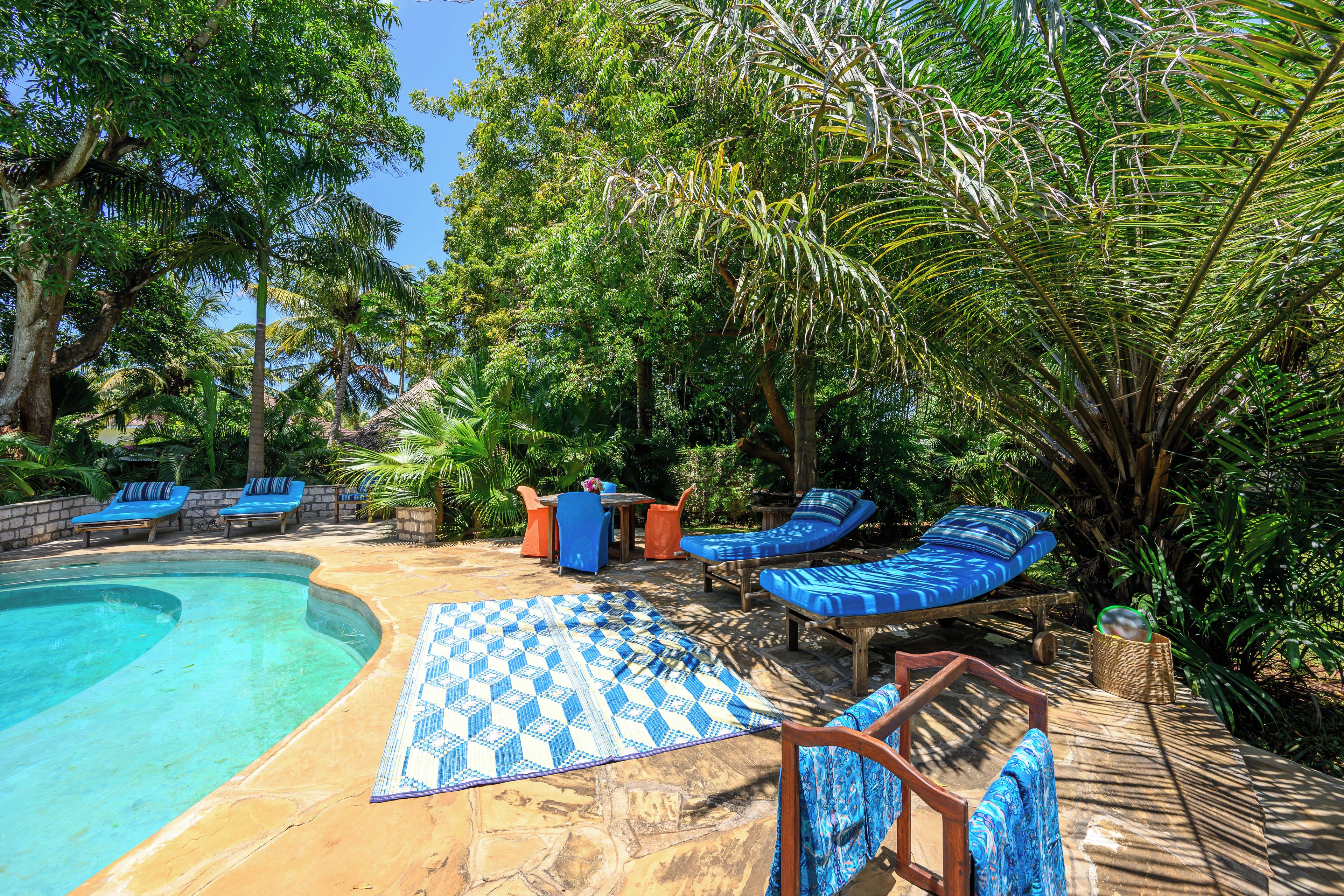 A pool area with lounge chairs and a table, surrounded by lush greenery.