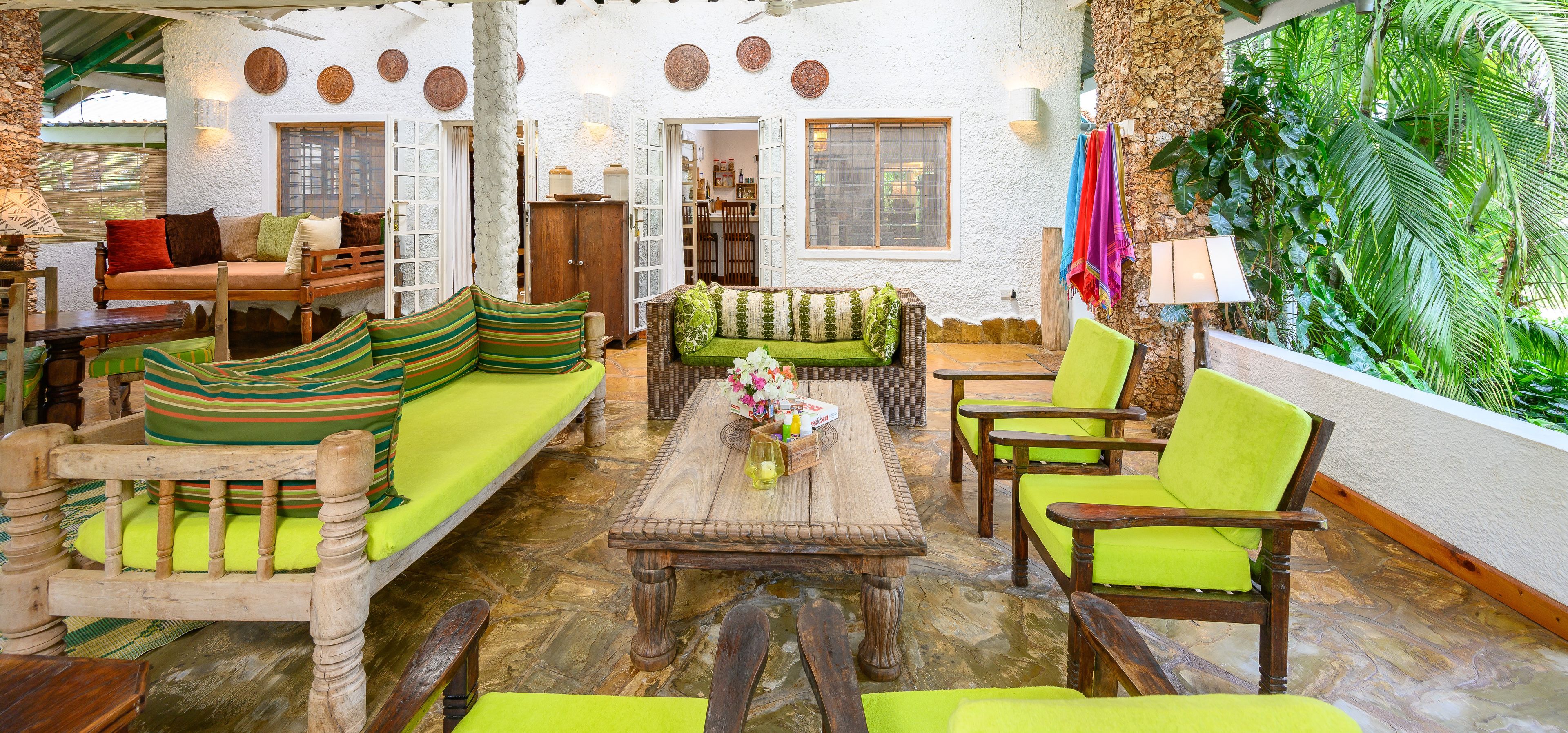 A cozy, well-lit interior with a seating area featuring wooden furniture and vibrant green cushions, a stone wall with a plant wall, and a rustic wooden table.