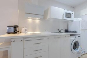 Eine moderne Küche mit weißen Schränken, einer eingebauten Mikrowelle, einer Kaffeemaschine und einer Waschmaschine.