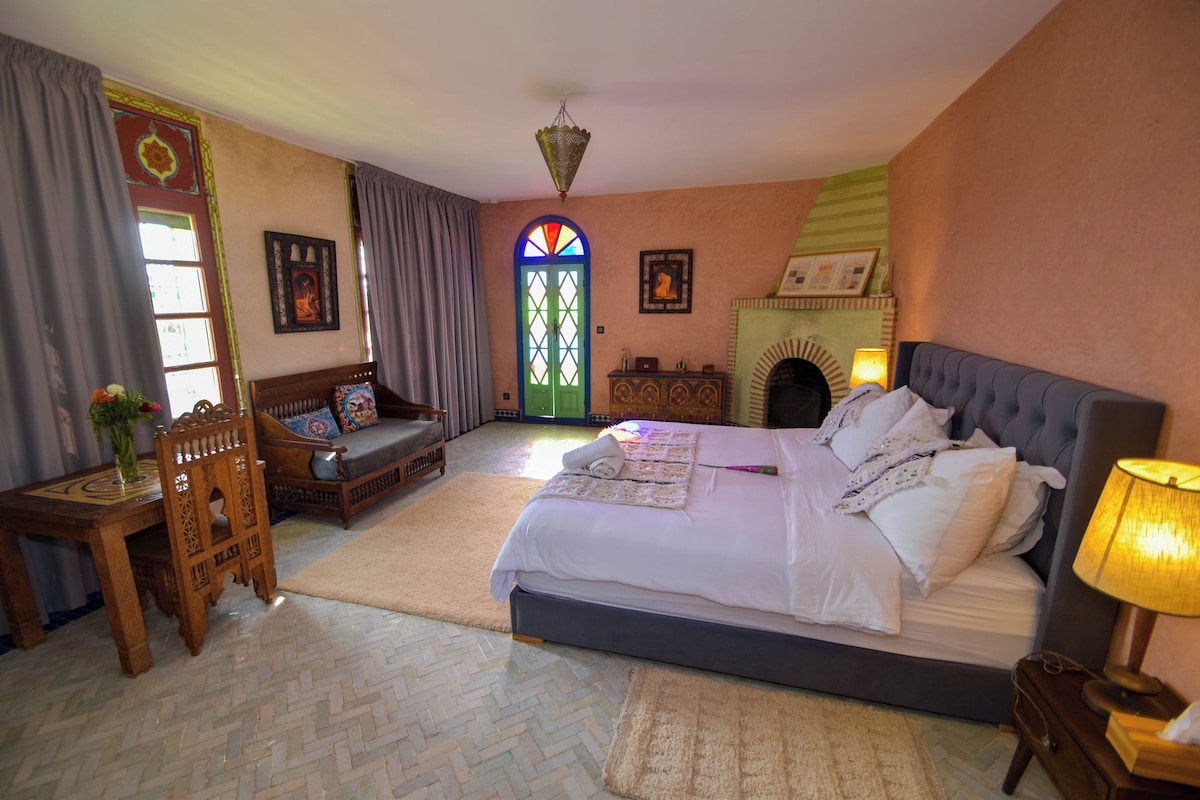 Une chambre à coucher avec un lit, un canapé, une table, une lampe et une cheminée.