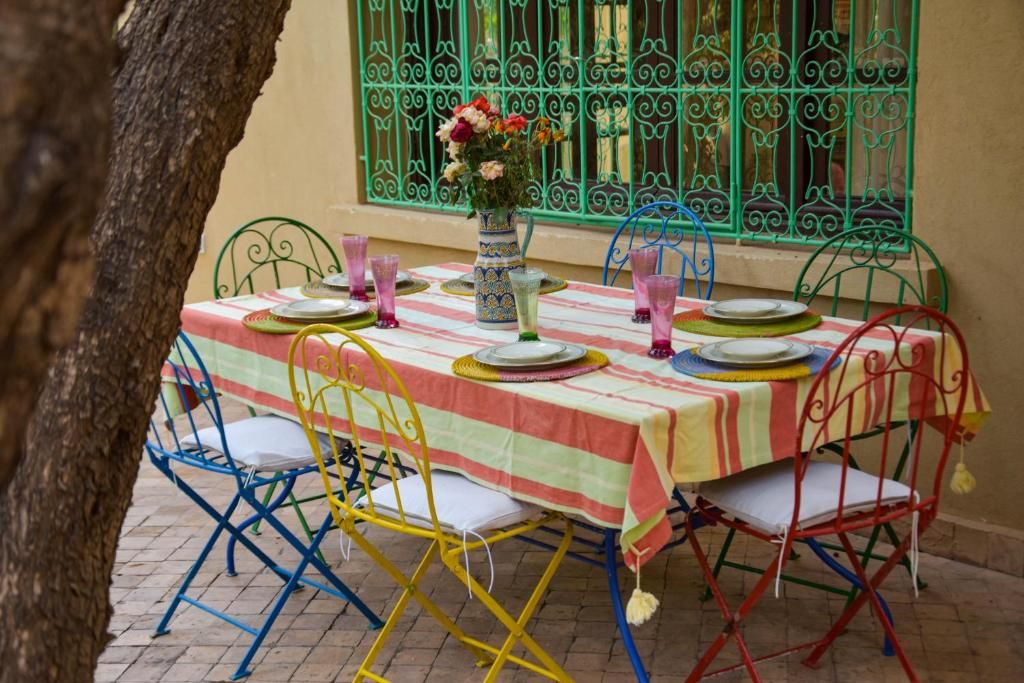 Una mesa para cuatro con mantel a rayas, sillas de metal y un jarrón con flores.