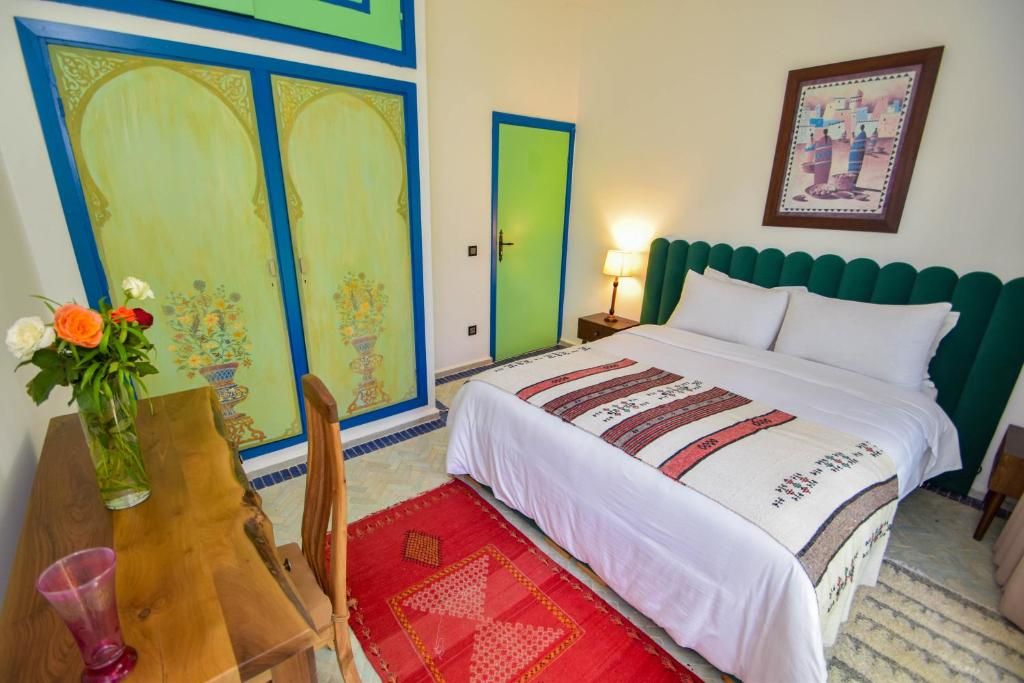 Una habitación con una cama, una mesita de noche, una mesa con un jarrón de flores y una puerta con marco verde.