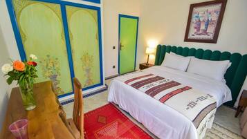 Una habitación con una cama, una mesita de noche, una mesa con un jarrón de flores y una puerta con marco verde.