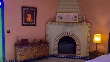 Una habitación con chimenea, una cama, una mesita de noche con lámpara y un mueble decorativo.