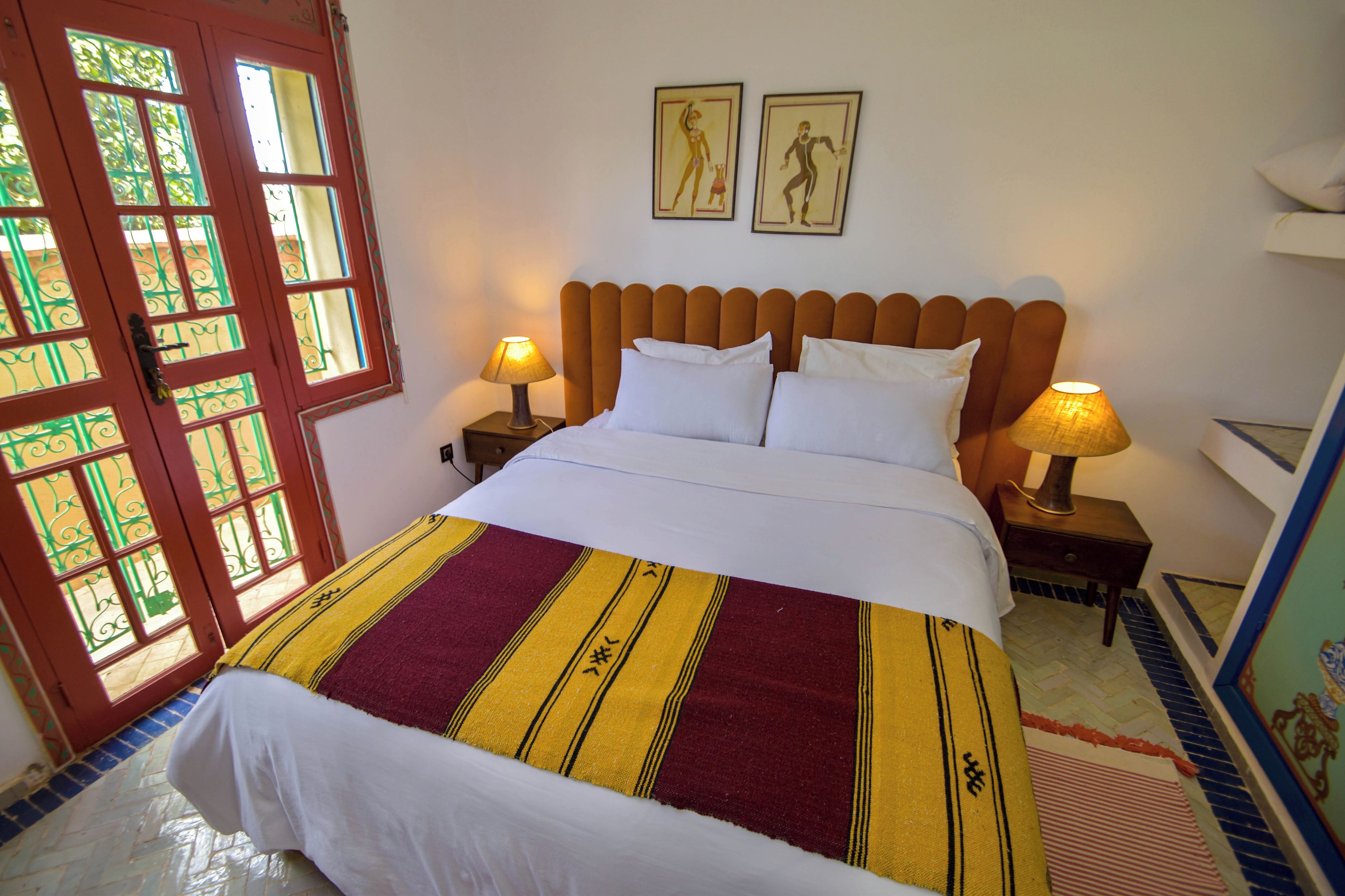 A bed with a striped bedspread, two bedside lamps, a headboard, and a door with decorative glass panels.