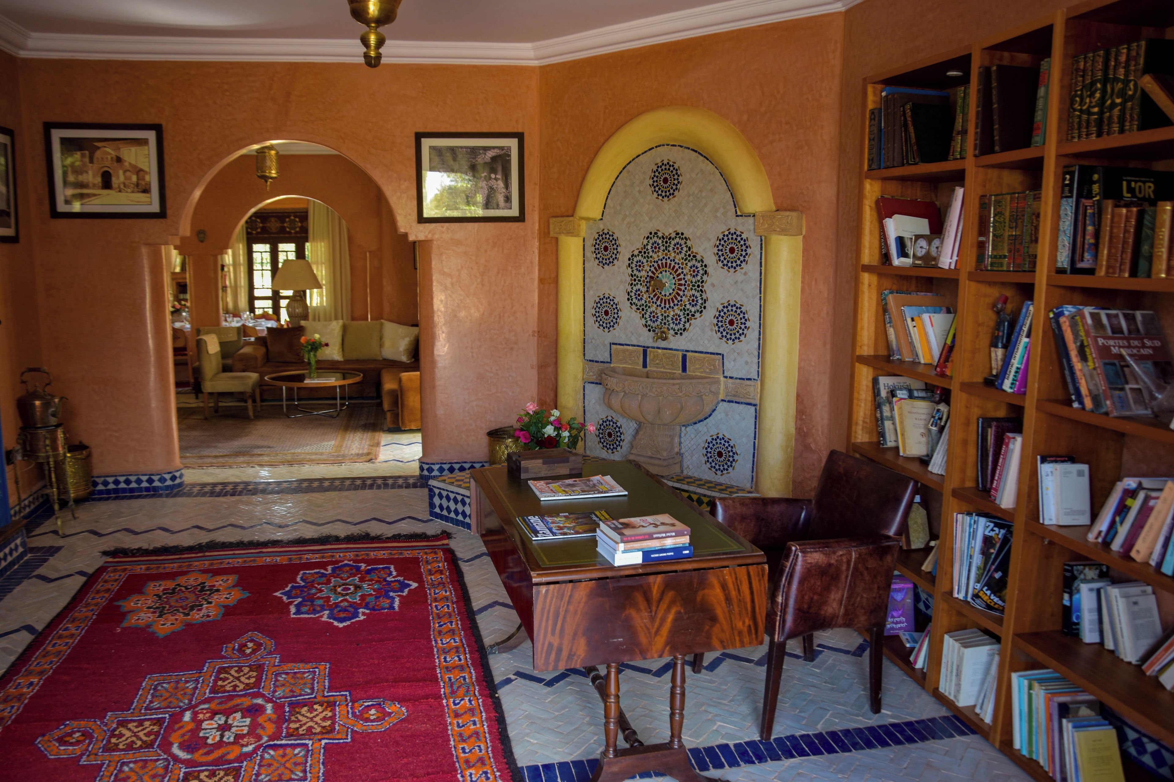 A room with a wooden desk, bookshelves, a patterned rug, and a decorative wall.
