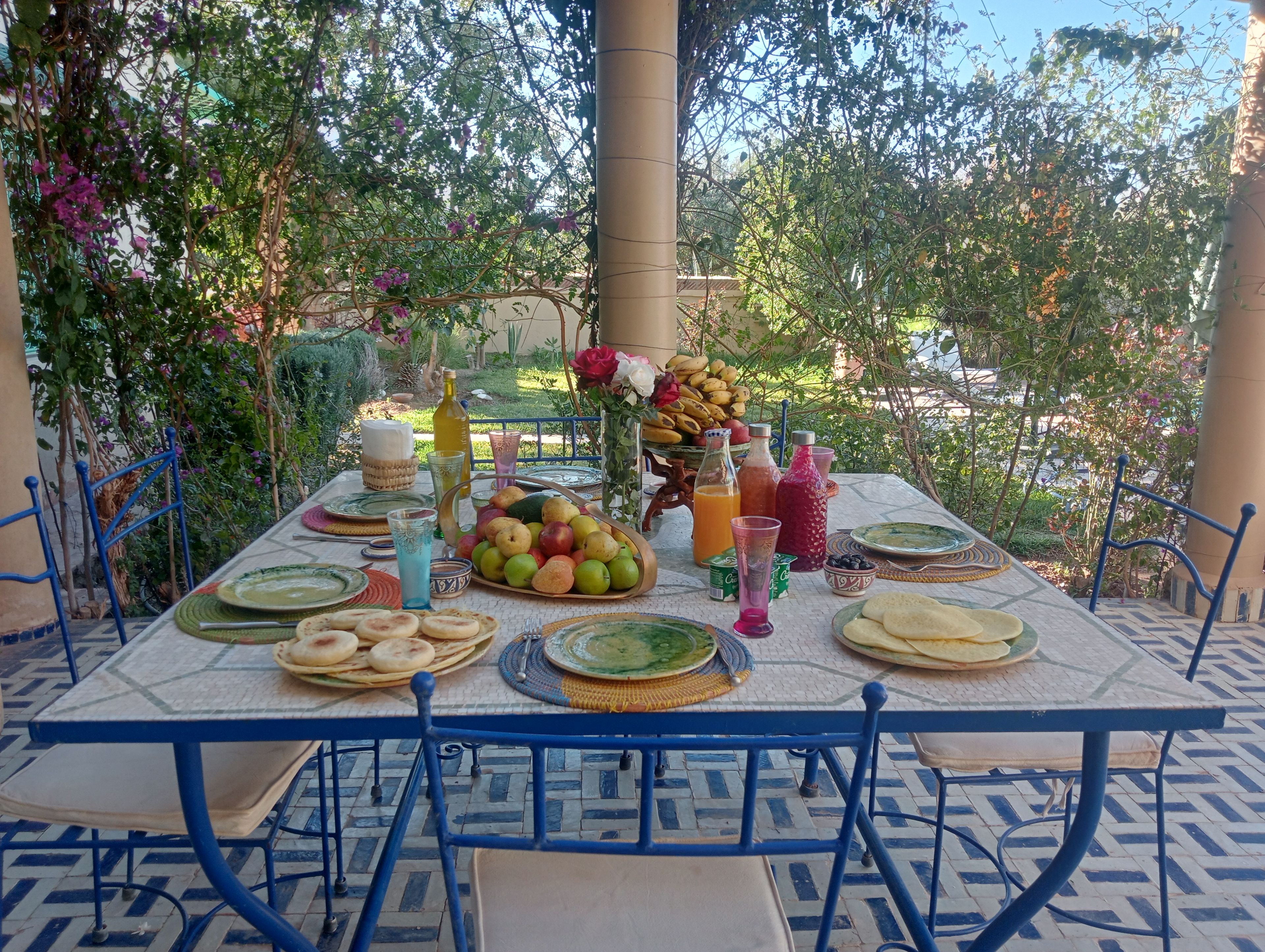 Un tavolo da pranzo all'aperto apparecchiato con piatti, bicchieri e una selezione di frutta e bevande.