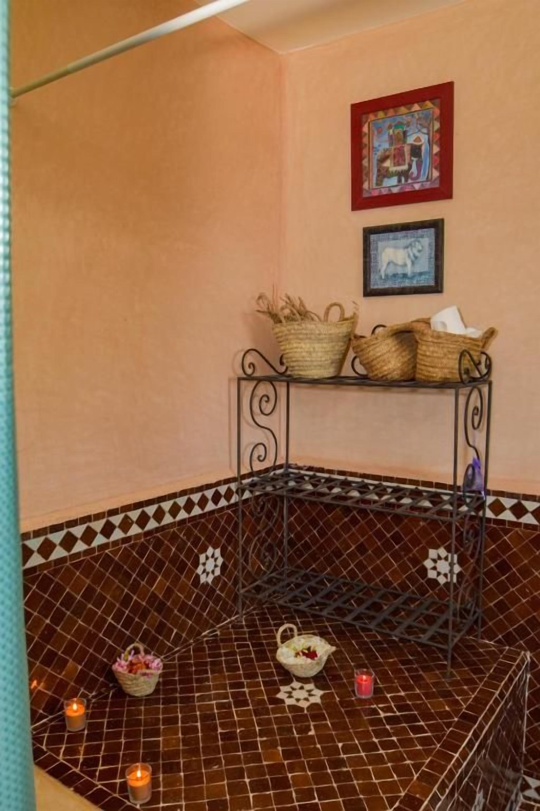 Una esquina de una habitación con suelo de baldosas, una estantería metálica con cestas y dos velas.