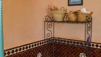 Una esquina de una habitación con suelo de baldosas, una estantería metálica con cestas y dos velas.