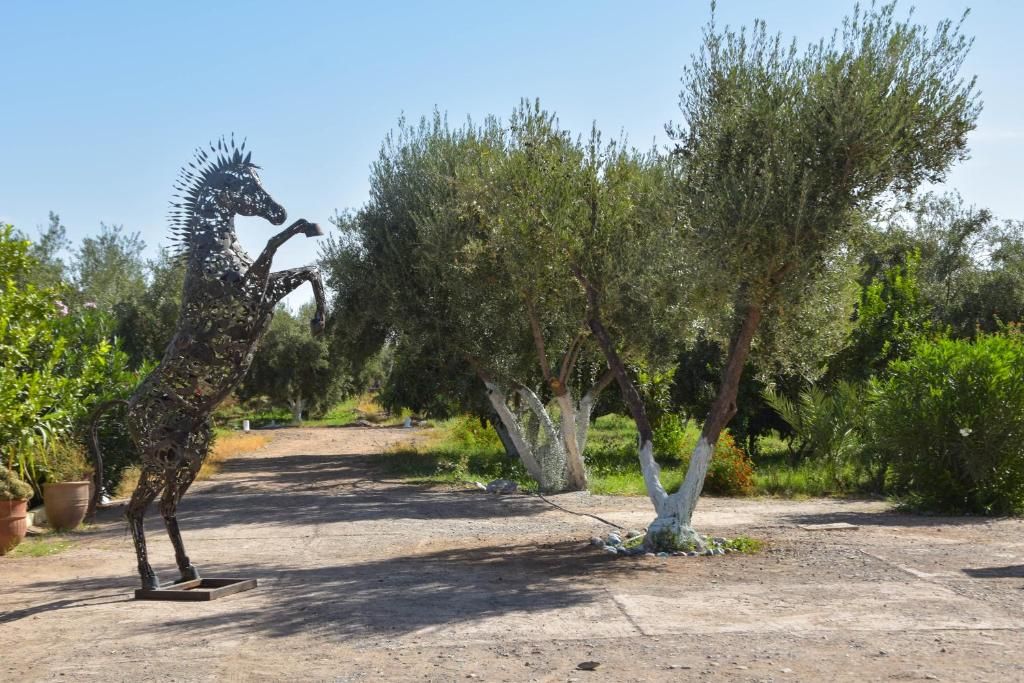 A metal sculpture of a horse in a natural setting with trees and a dirt path.