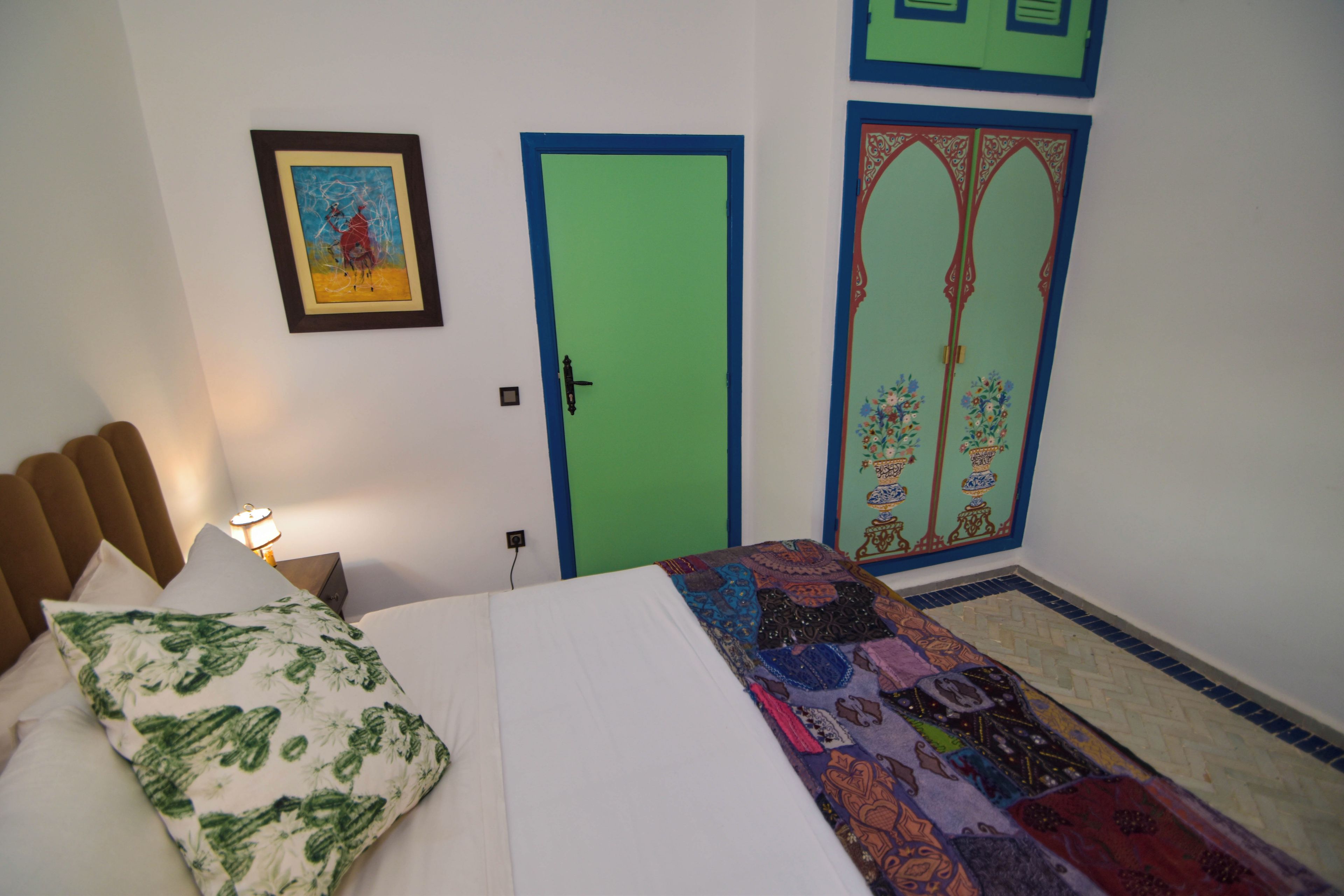 Un dormitorio con una cama, una mesita de noche, una lámpara, una puerta verde y un adorno en la pared.