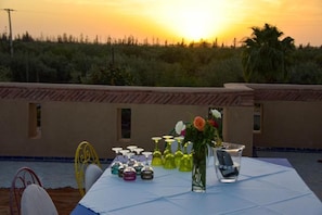 Une table dressée à l’extérieur, avec différents types de verres et un vase de fleurs, donnant sur un paysage naturel.