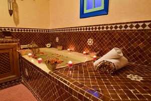 A bathroom with a tiled floor, a bathtub, candles, and towels.
