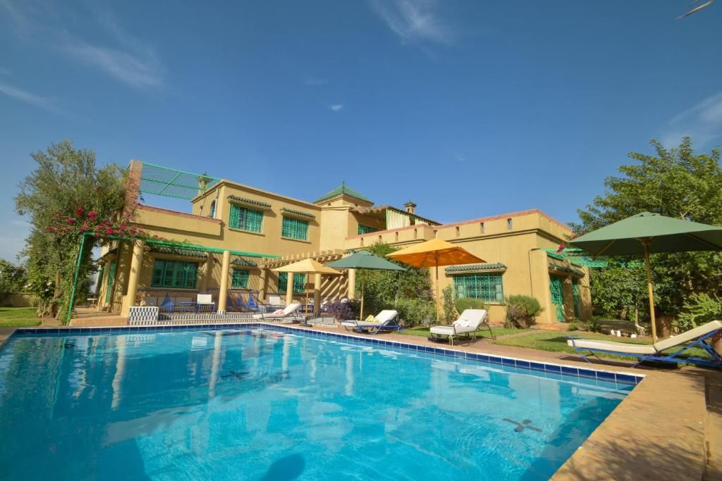 Ein Pool mit Liegestühlen und Sonnenschirmen, umgeben von einem Gebäude mit zahlreichen Fenstern und einer überdachten Terrasse.