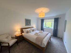 A bedroom with a bed, bedside table, chair, and a window with curtains. - The Cottage at Lundavra Farm (Lundavra)