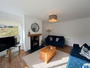 A modern living room with a television, a fireplace, a blue sofa, and a wooden coffee table. - The Cottage at Lundavra Farm (Lundavra)