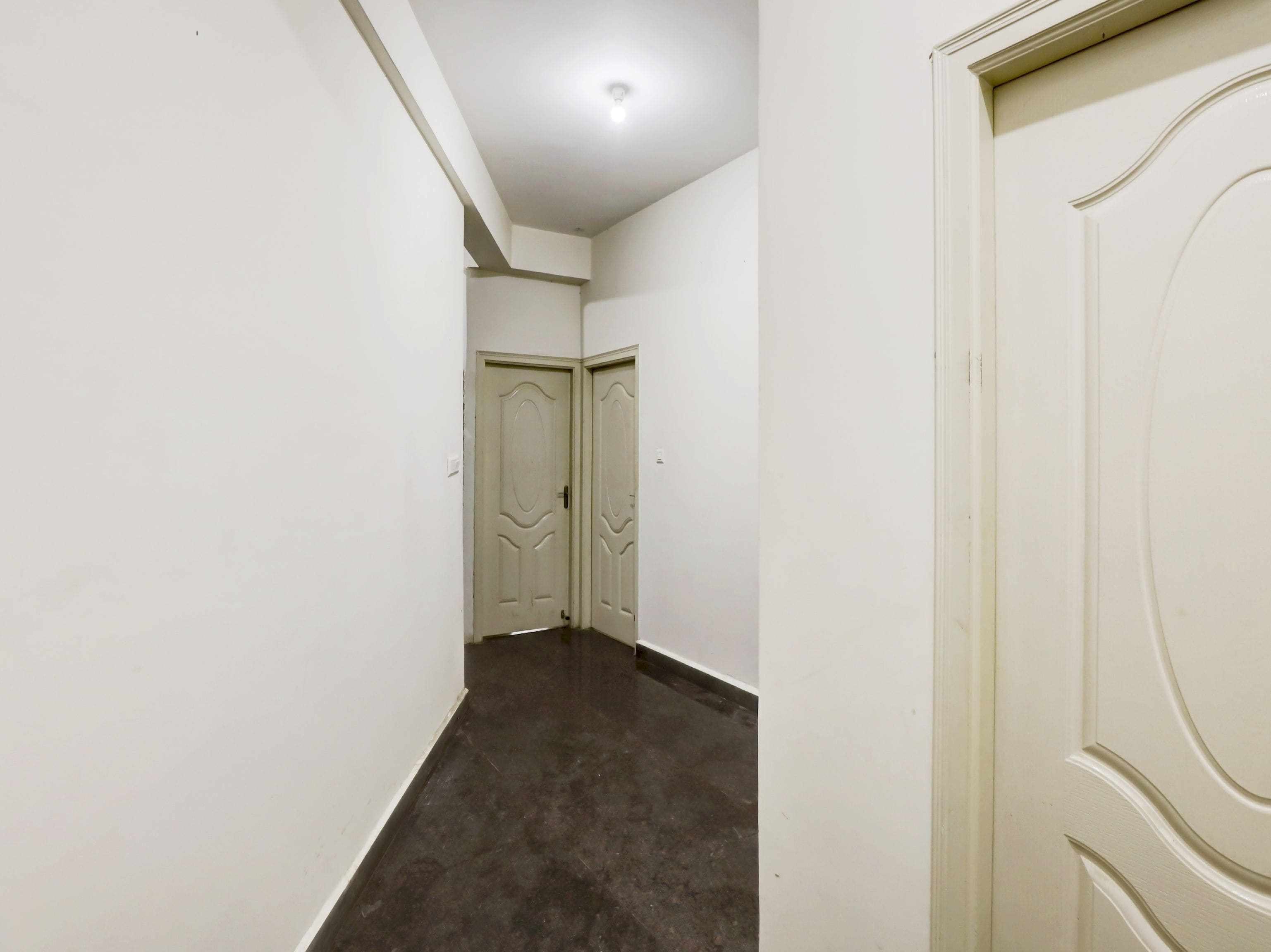 Un pasillo estrecho con dos puertas al final, una lámpara en el techo y un piso oscuro.