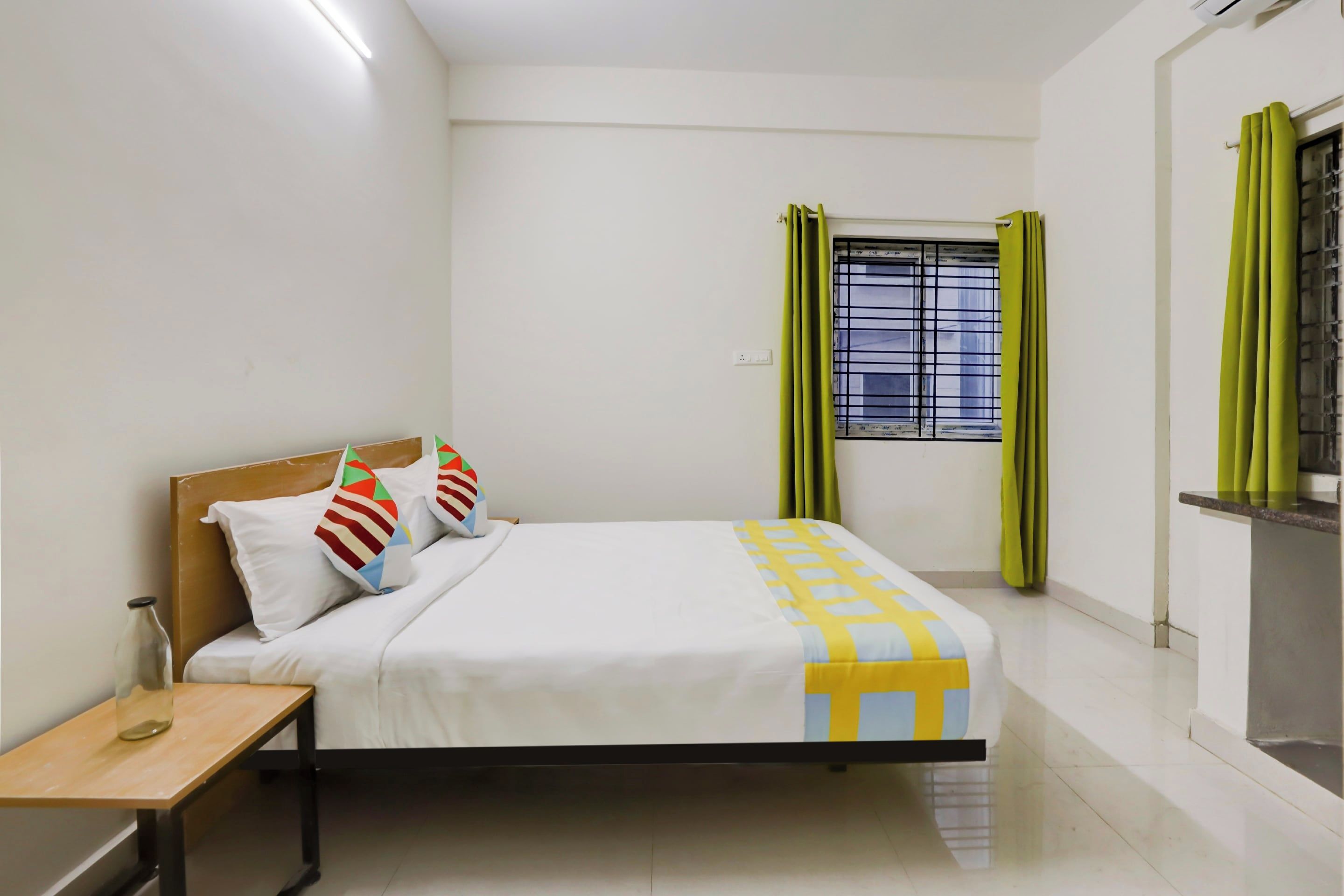 Un dormitorio con cama, mesita de noche, ventana con cortinas y aire acondicionado instalado en la pared.