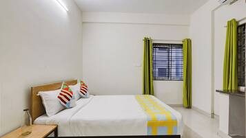 Un dormitorio con cama, mesita de noche, ventana con cortinas y aire acondicionado instalado en la pared.