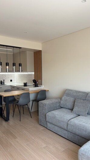 A modern living room with a grey sofa, a wooden dining table with chairs, and a kitchen area with a white countertop and black appliances. - Rio in Sight. Apartment in downtown Portimão with a view of the waterfront. (Portimão)