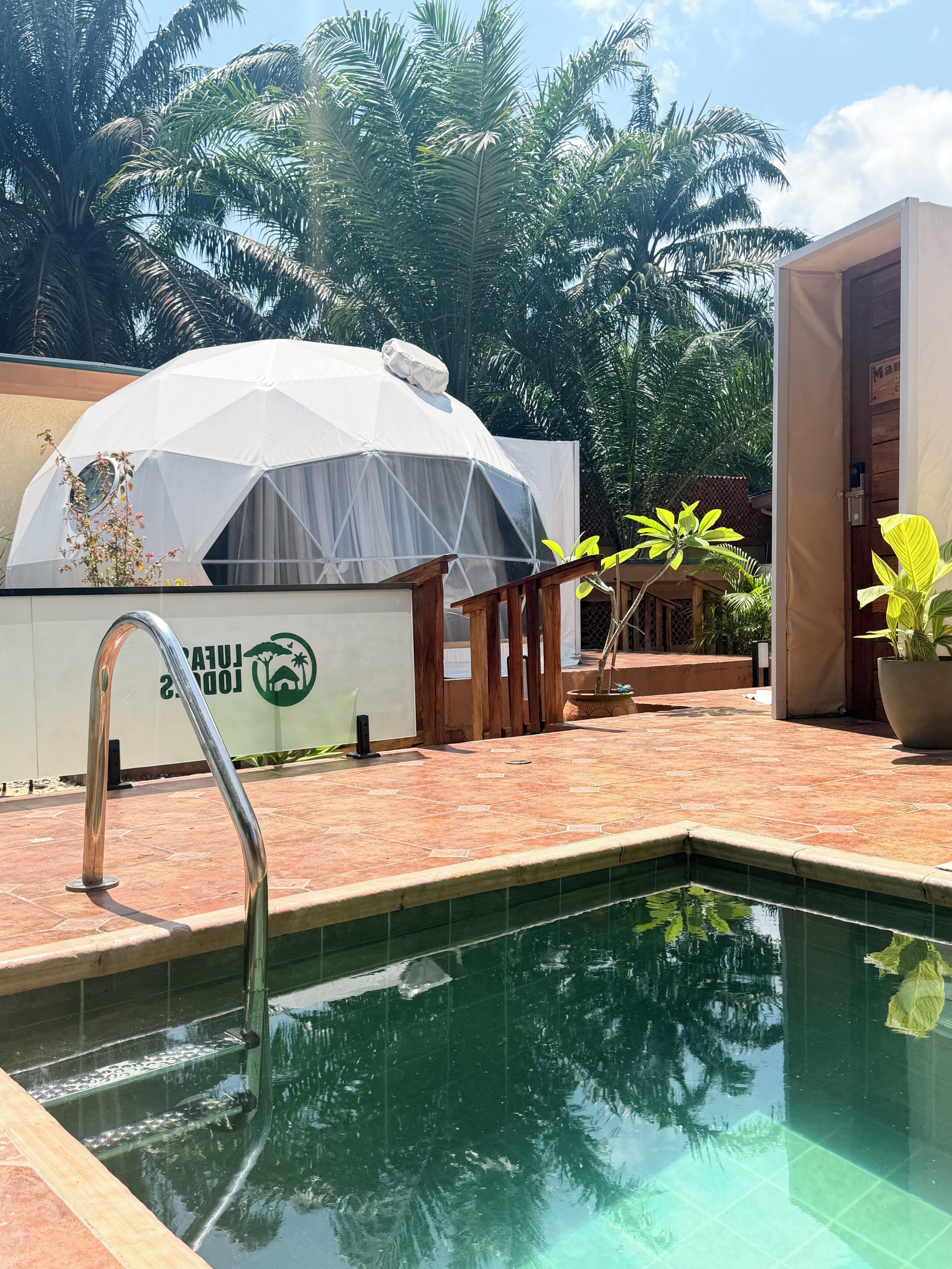 Uma piscina com escada de metal, uma estrutura em forma de tenda branca e um deck de madeira.