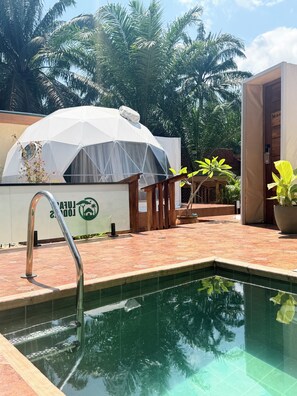 A swimming pool with a metal ladder, a white tent-like structure, and a wooden deck.