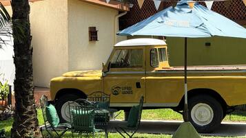 Veículo amarelo com a marca 'Lufasi Lodges' estacionado em área gramada, com móveis de exterior e uma palmeira.
