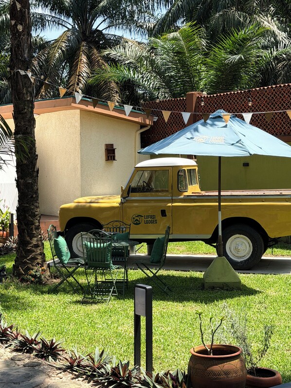 A yellow vehicle with 'Lufasi Lodges' branding parked in a grassy area with outdoor furniture and a palm tree.