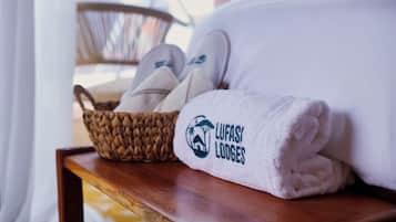 Une serviette soigneusement pliée, ornée d’un logo et d’un texte, un panier en osier contenant des chaussons et une table en bois.