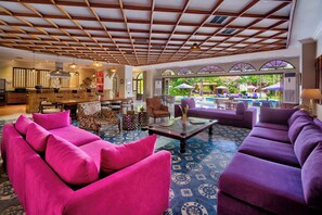 A spacious lounge area with a pool view, featuring vibrant purple sofas and a bar area with wooden accents. - Villa Sayang d'amour (Seminyak)