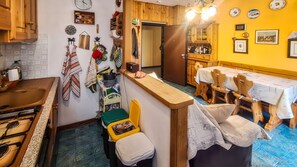 A kitchen with a stove, sink, and wooden cabinets. There is a dining area with a table and chairs. - GRAN PARADIS - Panoramic Apartment in Aprica / San Pietro (San Pietro)