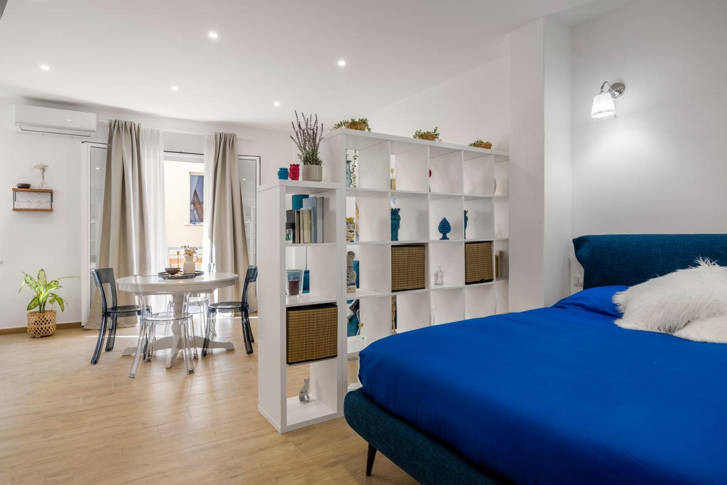 Une chambre moderne avec un lit bleu, une bibliothèque blanche et un coin repas comprenant une table et des chaises.