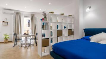 Une chambre moderne avec un lit bleu, une bibliothèque blanche et un coin repas comprenant une table et des chaises.