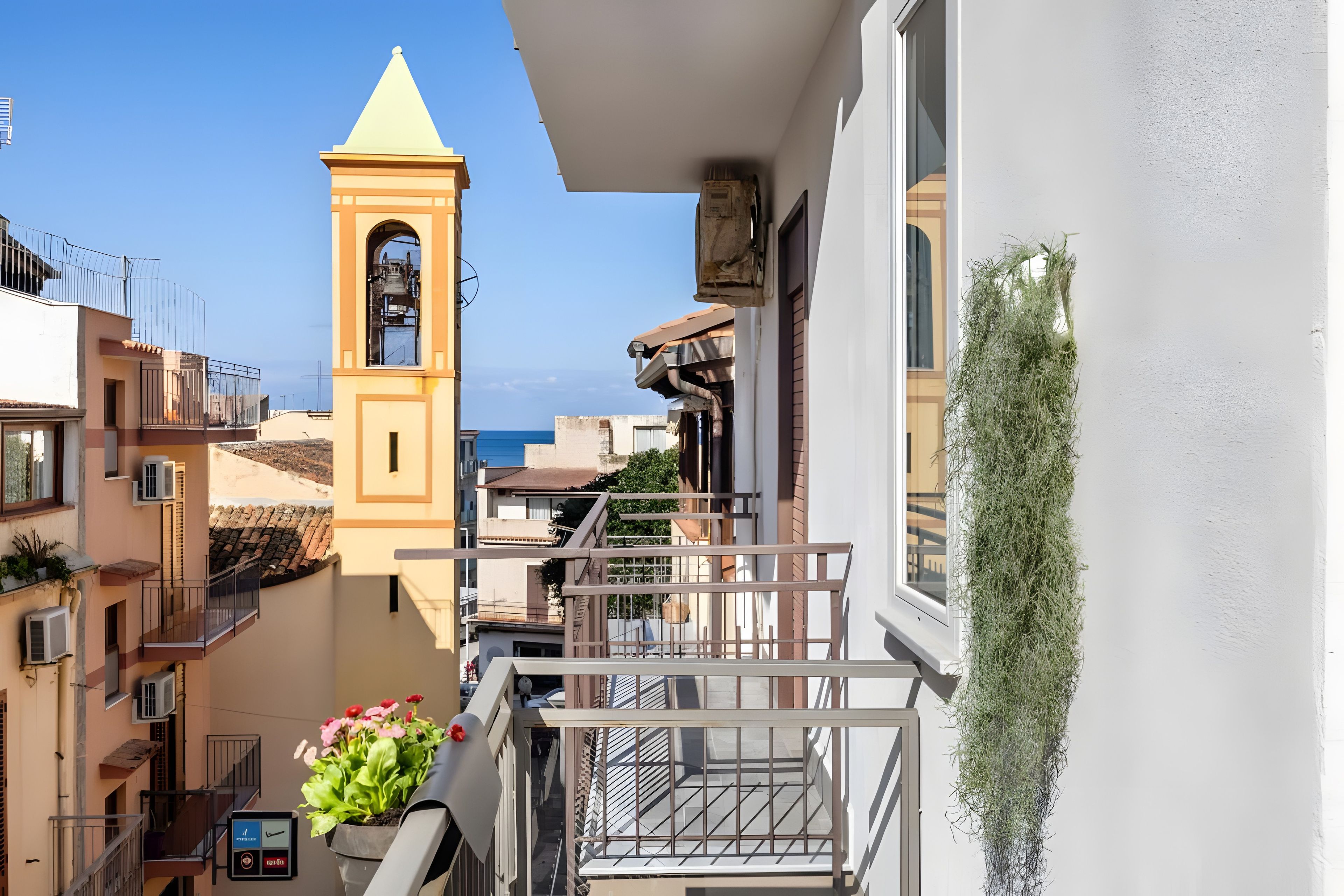Un balcon avec vue sur la mer, un clocher et un pot de fleurs.