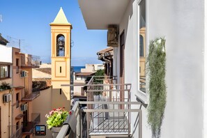 Ein Balkon mit Blick auf das Meer, ein Glockenturm und ein Blumentopf.