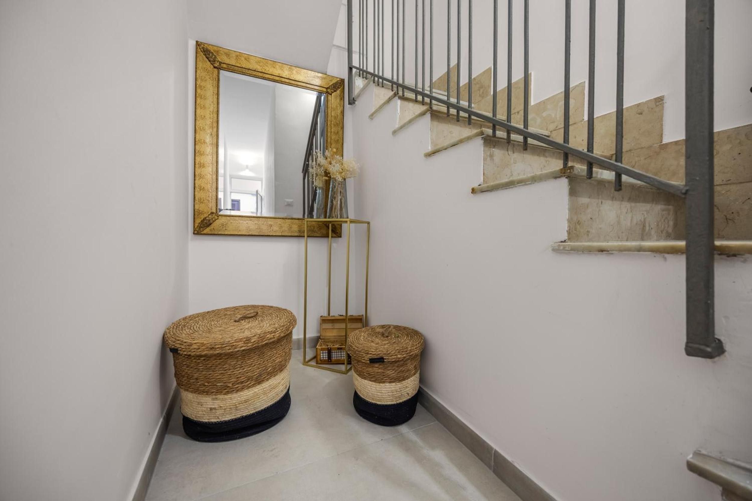 Eine Treppe mit Metallgeländer, ein großer Spiegel mit goldener Rahmung und zwei gewebte Körbe auf dem Boden.