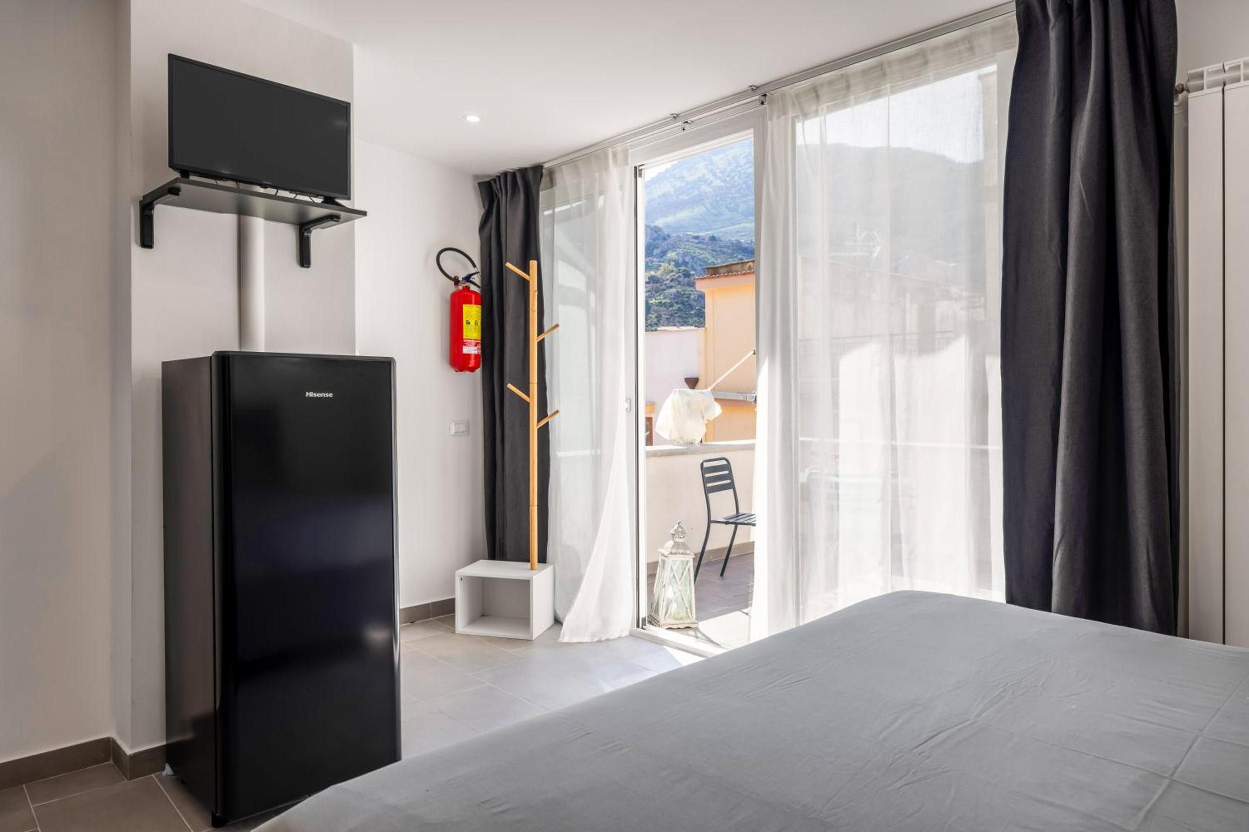 Une chambre d’hôtel avec un lit, un téléviseur fixé au mur, un extincteur et une vue sur le balcon extérieur.