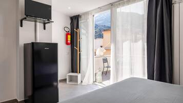 Une chambre d’hôtel avec un lit, un téléviseur fixé au mur, un extincteur et une vue sur le balcon extérieur.