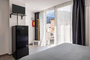 Ein Hotelzimmer mit Bett, einem an der Wand montierten Fernseher, einem Feuerlöscher und Blick auf den Außenbalkon.
