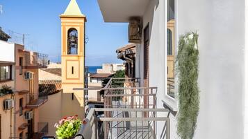 Un balcon avec vue sur la mer, un clocher et un pot de fleurs.