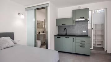 Une chambre compacte comprenant un lit, une kitchenette et une salle de bain.